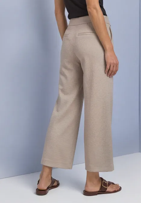 High Waist Culotte im Casual Fit saddle brown Frau trägt beigefarbene, weit geschnittene Culotte-Hose und braune Sandalen, Rückansicht.