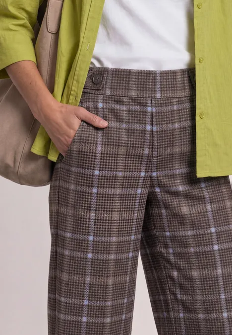 Person trägt karierte braune Hose, weißes Top, grünes Hemd und eine Schultertasche.