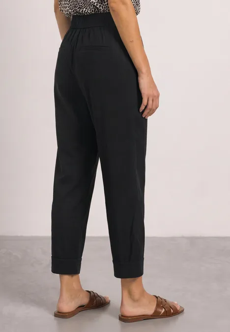 Achteraanzicht van iemand in een zwarte, opgerolde broek met bruine sandalen.