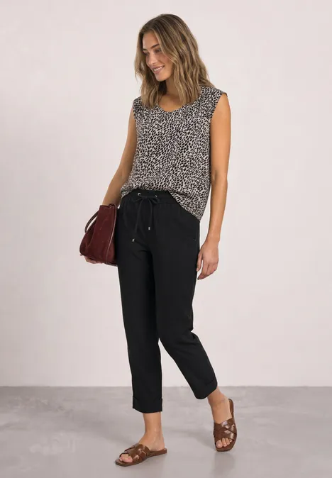 Vrouw met mouwloze top met print, zwarte broek, bruine sandalen en een rode schoudertas.