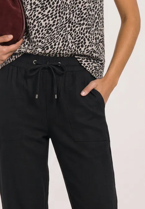 Vrouw met zwarte broek met koord, luipaardtop en bordeaux clutch.