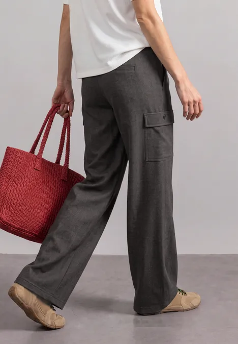 Pantalon Straight Leg avec poches cargo black coffee Frau in weiten grauen Stoffhosen, weißem Oberteil und beigen Sneakers hält roten Korb-ähnlichen Shopper.
