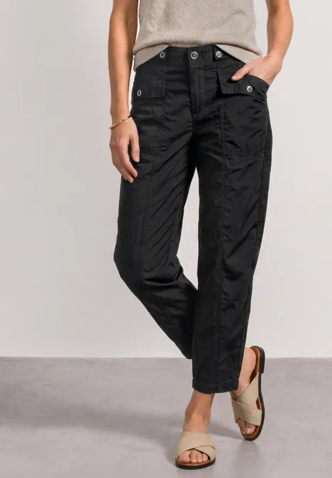 Femme portant un pantalon noir droit taille haute jusqu'aux chevilles, fermé par boutons-pression, avec sandales.
