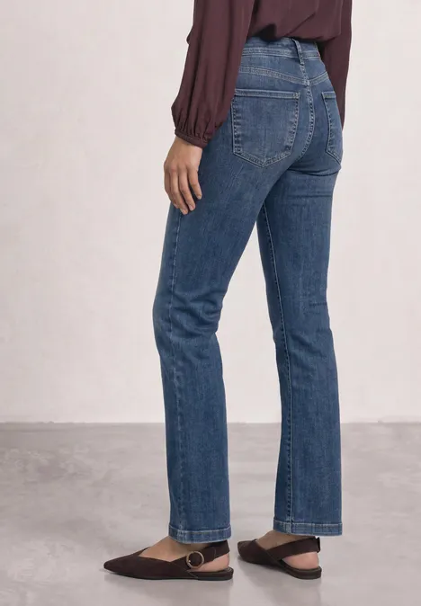 Eine Person trägt gerade geschnittene blaue Jeans und eine burgunderrote Bluse.