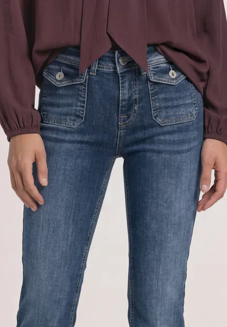 Nahaufnahme einer Person in dunkelblauen Jeans mit großen vorderen Hosentaschen und roter Bluse