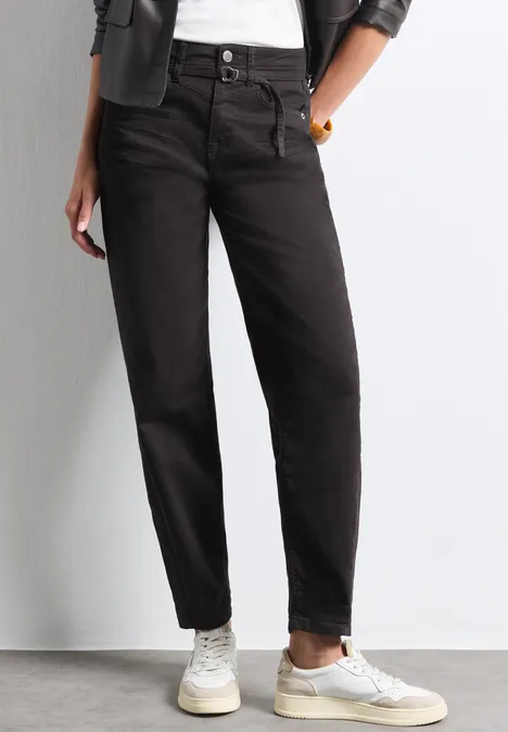 Frau trägt schwarze High-Waist-Jeans, weiße Sneaker, weiße Socken, weißes T-Shirt und schwarze Jacke.