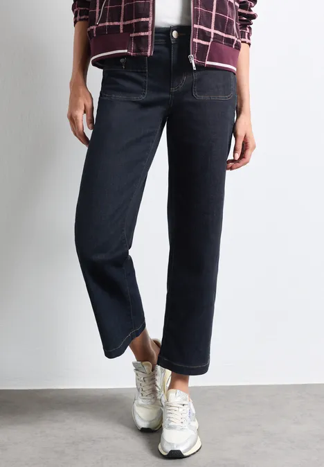 Mid Waist Straight Leg Jeans im Casual Fit Rinse Washed Person trägt dunkle, gerade geschnittene Jeans und weiße Sneakers, stehende Pose auf grauem Untergrund.