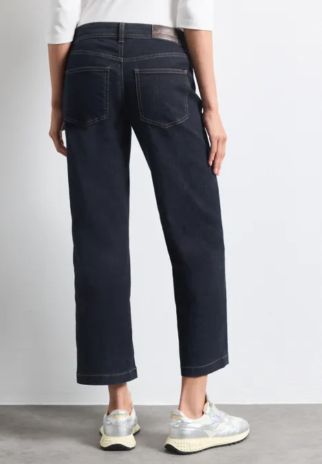 Mid Waist Straight Leg Jeans im Casual Fit Rinse Washed Eine Person von hinten in dunklen, geraden Jeans und weißen Sneakern.