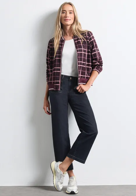 Mid Waist Straight Leg Jeans im Casual Fit Rinse Washed Frau mit Karo-Jacke, weißem Top, weiter Jeanshose und weißen Sneakern.