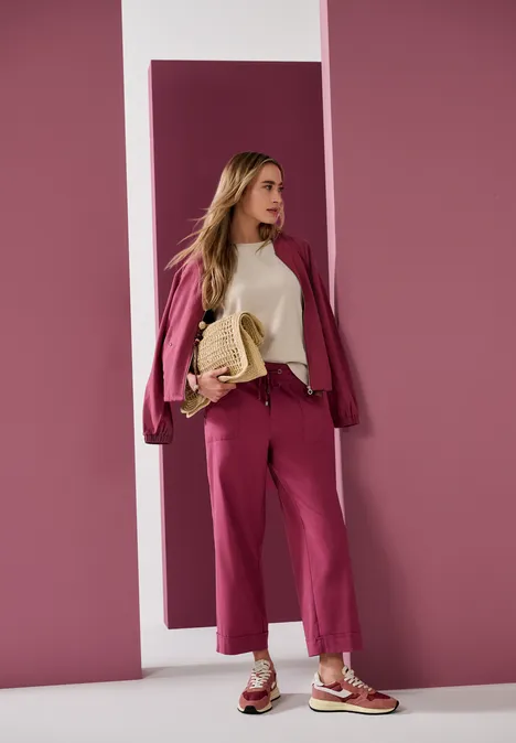 Straight Leg Hose im Casual Fit mit Turn-Up dark clouded blush Frau in pinkem Hosenanzug, weißem Top und passenden Turnschuhen mit Tasche vor rosa Hintergrund.