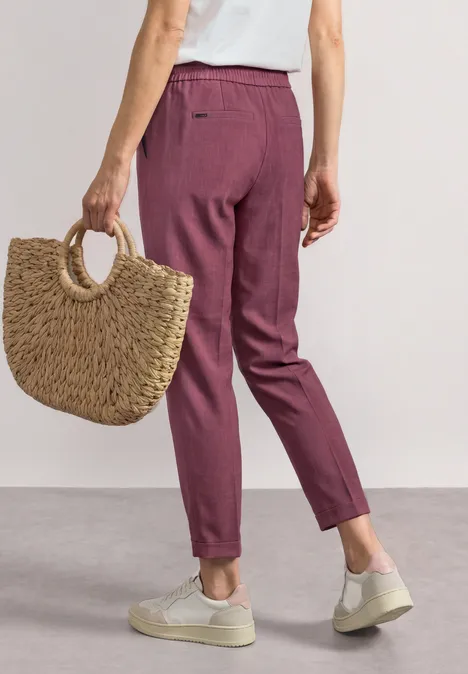 Femme en pantalon de tailleur bordeaux, baskets blanches, tenant un panier en paille.