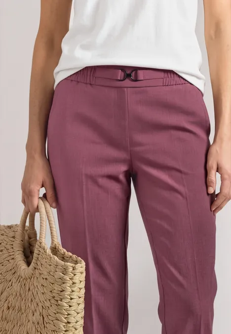 Une personne porte un top blanc, un pantalon prune et tient un panier en paille.