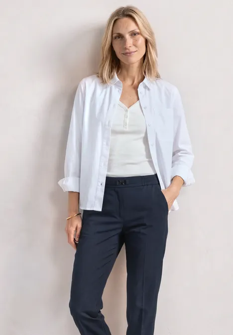 Slim Leg Hose mit Schnallendetail darkest blue Frau in weißem Hemd, weißem Top und dunkelblauen Hosen vor neutralem Hintergrund.