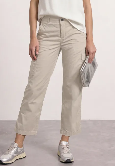Beine in beigen Culotte-Hosen, weißem Top, silbernen Sneakern und silberner Clutch