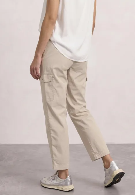 Femme vue de dos/latéral portant un pantalon cargo beige, un top blanc et des baskets claires.