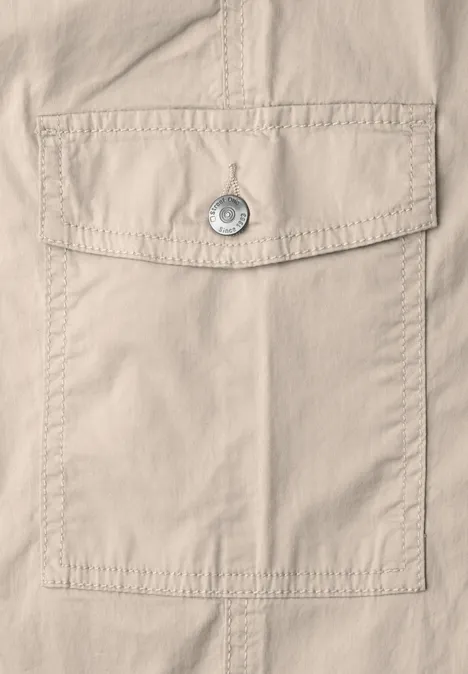 Gros plan d’une poche en tissu beige avec rabat, bouton-pression et surpiqûres apparentes.
