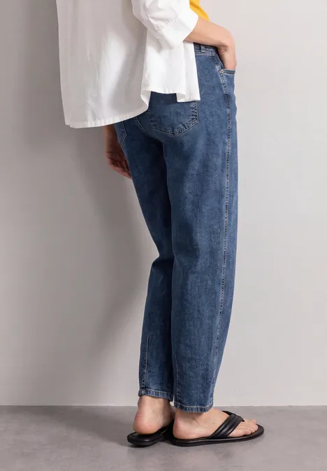 Seitliche Ansicht einer Person mit weiten blauen Jeans, weißem Oberteil und schwarzen Sandalen.
