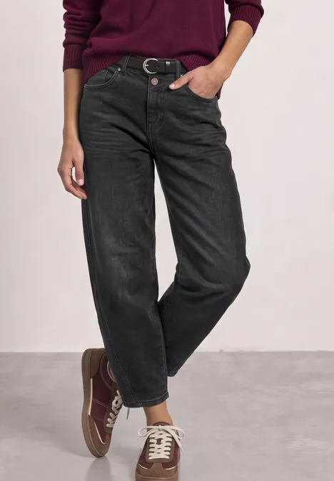 Vrouw draagt een bordeauxrode trui, zwarte wijde jeans en bijpassende sneakers.