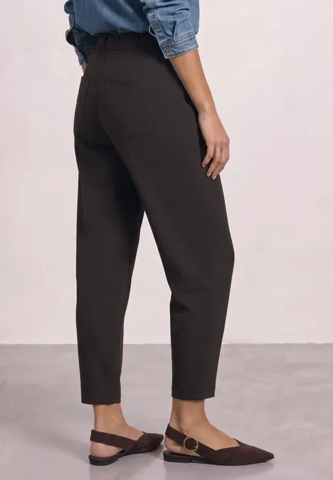 Knöchellange, schwarze Hose mit geradem Schnitt, kombiniert mit flachen, braunen Slingback-Schuhen.