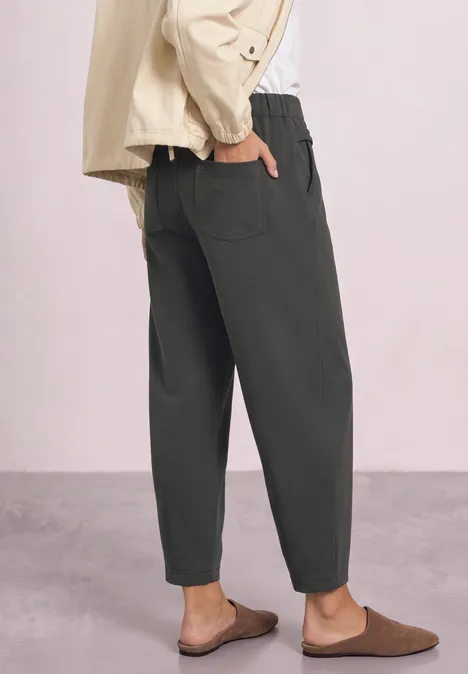 Frau in locker sitzender, olivgrüner Hose mit hoher Taille, seitlichen Taschen und braunen Hausschuhen.