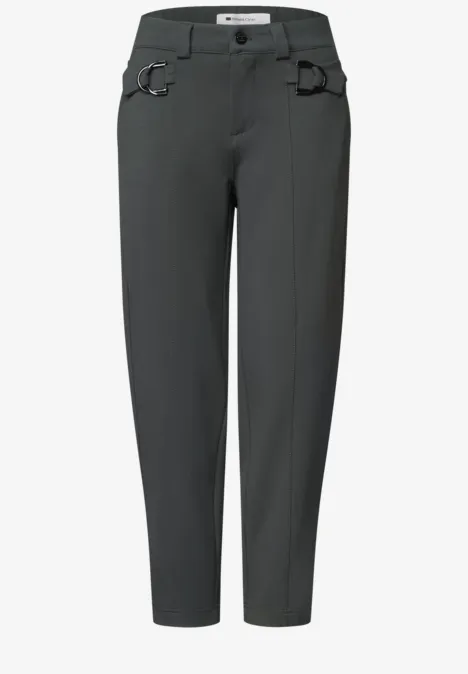 Dunkelgraue, lässige Hose mit leicht zulaufenden Beinen, Gürtelschlaufen und markanten Metallringen an den Taschen.
