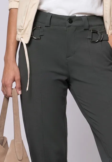 Frau trägt dunkelgraue Hose mit D-Ring-Details und beiger Tasche, lässiger Chic