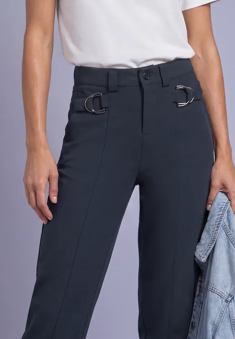 Person trägt weiße Bluse und dunkelblaue, elegante Hose mit D-Ringen am Bund, hält Jeansjacke.