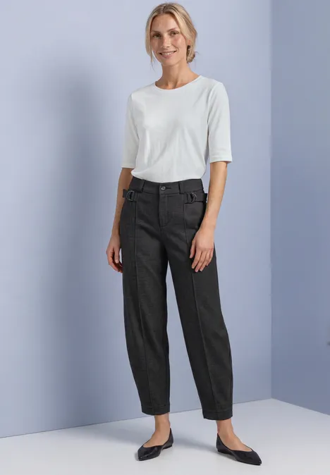 Barrel Leg Hose mit Schnallendetail black coffee Eine Frau steht in einer schlichten Umgebung, trägt ein weißes T-Shirt, graue Hose und schwarze Ballerinas.