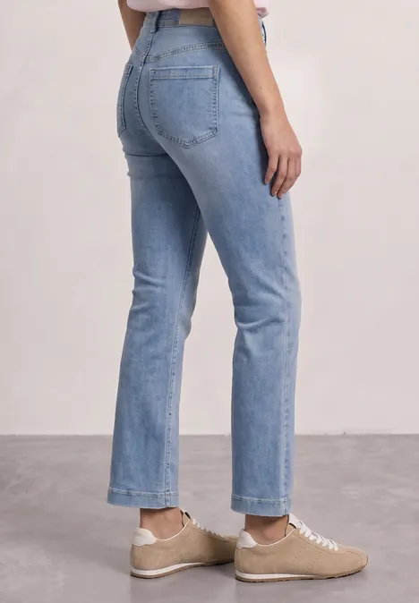 Zij-aanzicht van een vrouw in lichtblauwe, enkelhoge jeans en beige sneakers.
