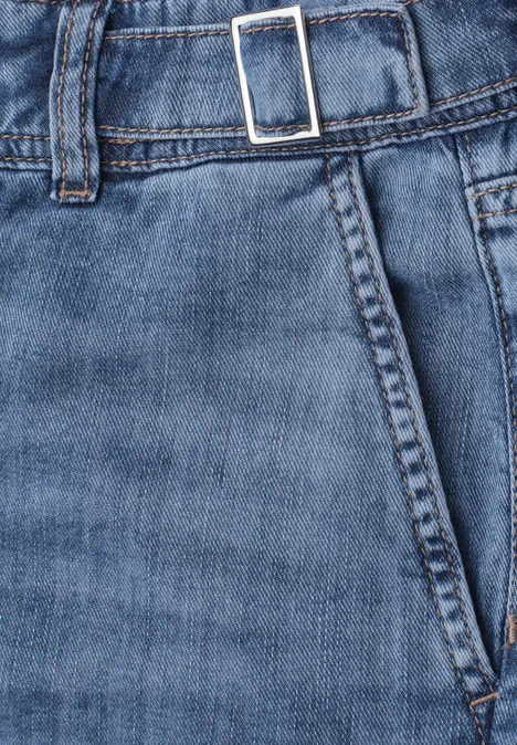 Close-up van een blauwe spijkerbroek met zak, tailleband en zilverkleurige gesp.