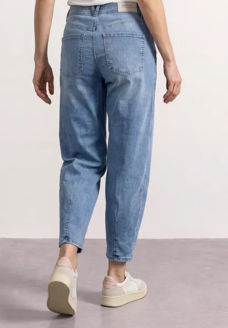 Vrouw van achteren in losse lichtblauwe spijkerbroek en witte sneakers.