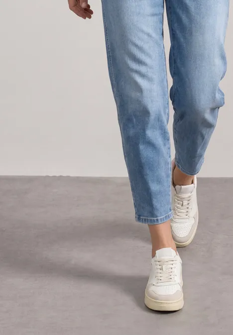 Een persoon loopt over een grijze vloer in lichtblauwe jeans en witte plateau-sneakers.