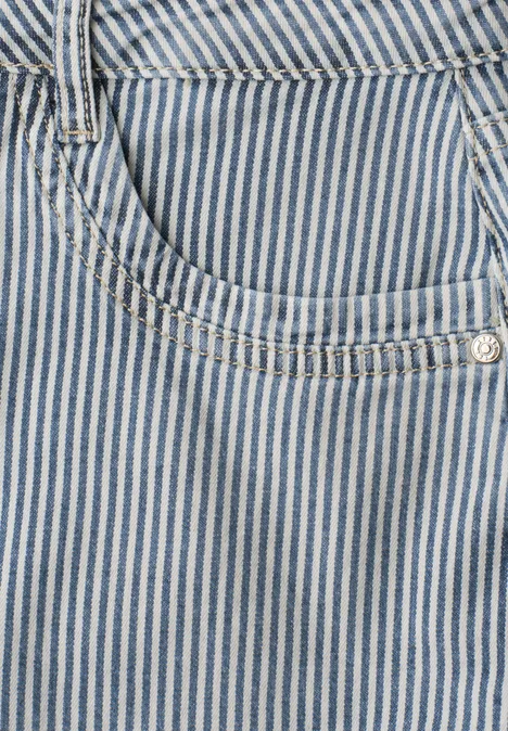 Gros plan d'une poche en denim bleu à fines rayures blanches, avec rivet argenté et coutures décoratives.