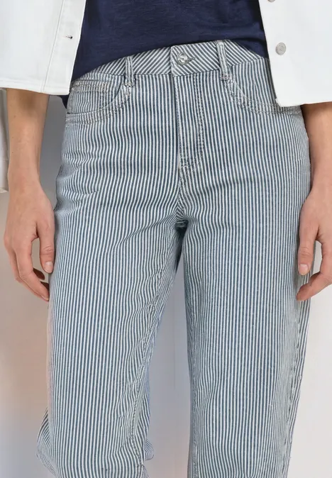 Personne porte un jean à rayures bleu et blanc taille haute, associé à un top bleu marine et une veste blanche.