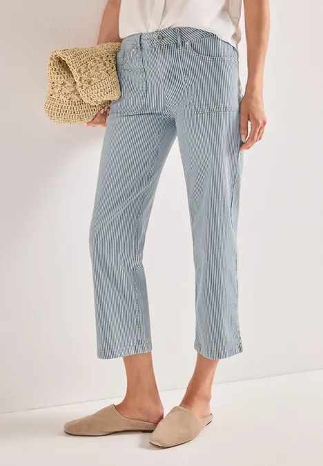 Une personne porte un jean bleu clair court, des mocassins beiges et tient un sac en paille.