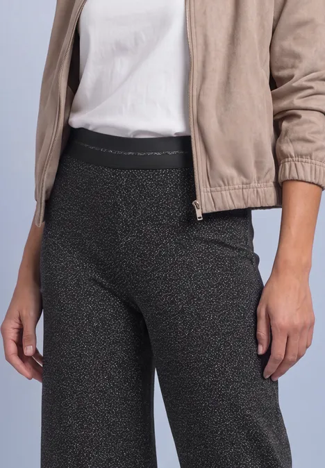 Persoon in beige jack, wit shirt en donkere, glinsterende legging.