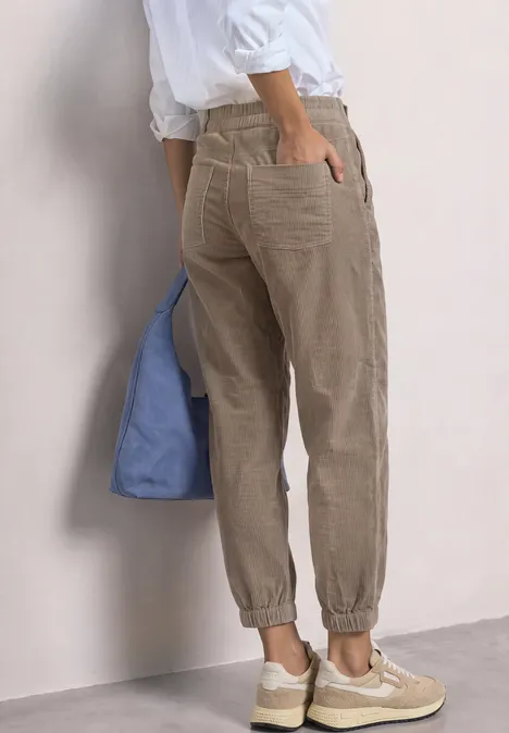 Une personne porte un pantalon en velours beige, des baskets blanches et un sac bleu.