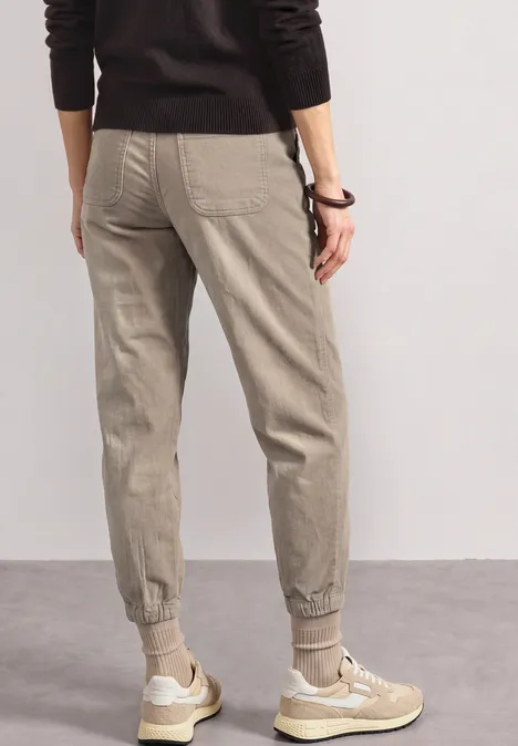 Spodnie High Waist z nogawkami typu barrel z elastycznym pas fading sand Osoba tyłem w jasnoszarych spodniach dresowych ze ściągaczami i beżowych sneakersach