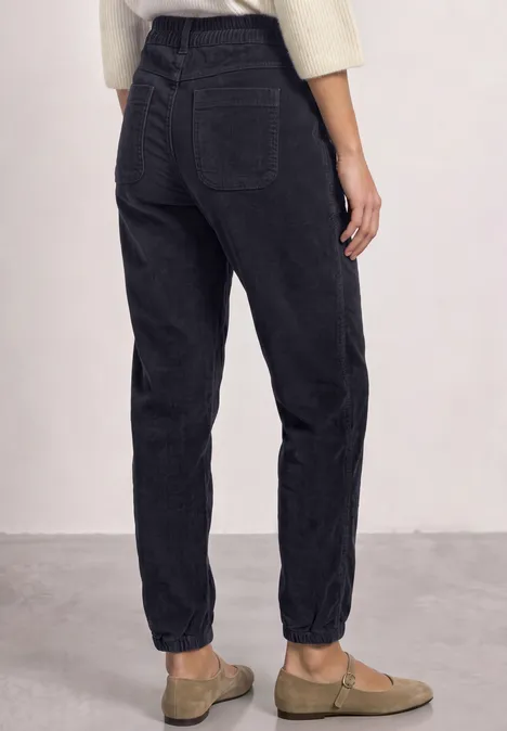 Rückansicht einer Person in schwarzen, hoch taillierten, lässigen Jeans mit aufgerolltem Saum und beige Slippern.