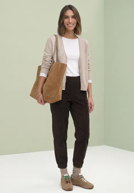 Vrouw met beige vest, wit shirt, donkere broek, bruine enkellaarzen en een bruin schoudertasje.
