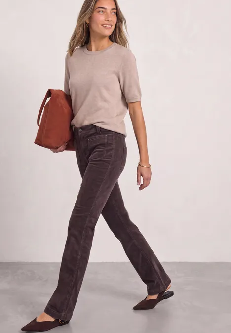 Pantalon bootcut taille haute à coupe ajustée ruby vine Frau in beigem Oberteil, dunklen Cordhosen und schwarzen Ballerinas, hält braune Tasche und geht lächelnd.