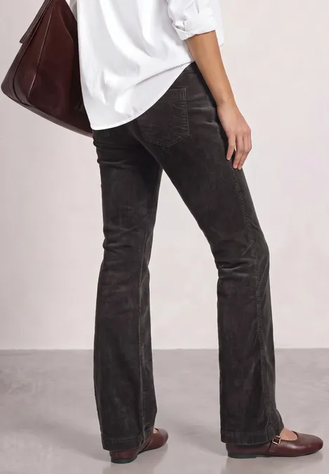Beine in dunkelbrauner Cord-Schlaghose, dazu weißes Hemd, braune Loafer und große Tasche.