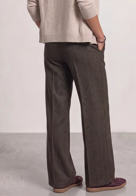 Person von hinten in beiger Strickjacke und weiten braunen Hosen