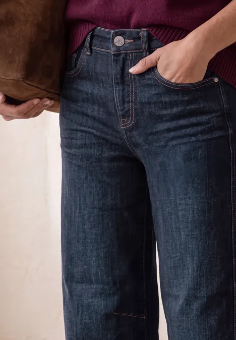 Jeans met High Waist en wijd uitlopende pijpen in een Loose Fit pasvorm Dark Blue Washed Nahaufnahme einer Person in weiten, hochgeschnittenen dunkelblauen Jeans, Hand in der Tasche und brauner Schultertasche