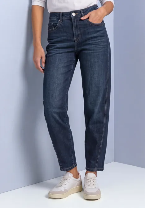 Hoch geschnittene, dunkelblaue Damenjeans mit schmaler Passform, leicht gekrempelt, kombiniert mit weißen Sneakern.