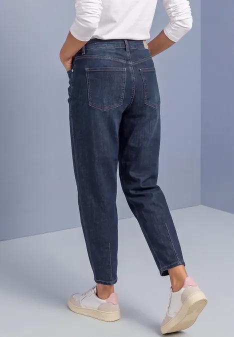 Rückansicht einer Person in dunklen Jeans und weißen Sneakern vor schlichtem Hintergrund.