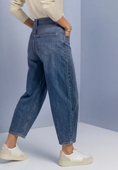 Jeans met High Waist en rechte pijpen in een Loose Fit-pasvorm Medium Blue Soft Washed Seitlich stehende Person in weiten blauen High-Waist-Jeans und weißen Sneakern, Hände in den Taschen.