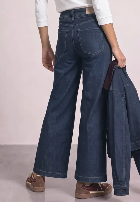Wide Leg Jeans mit Gürteldetail Dark Blue Washed Hoch geschnittene, weite Jeans mit weitem Bein, von hinten, Hand hält passende Jeansjacke.