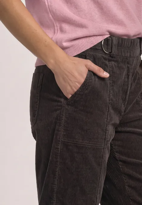 Bruine ribfluwelen broek met hand in zak, gecombineerd met een roze top.