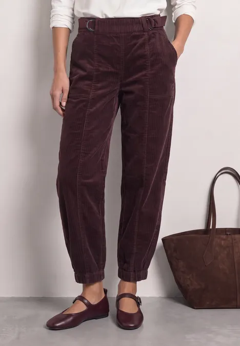 Dunkelrote Cordhose mit hohem Bund, lockerer Passform und elastischen Umschlagsäumen, kombiniert mit Mary-Jane-Schuhen.